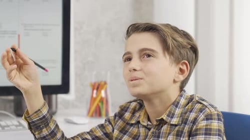 Boy Thinking and Working at Computer With Pencil