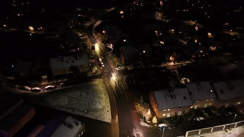 Aerial flyover snowy winter neighborhood at night. American town with parking cars at night. Warm li