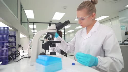 Focused Woman Using Microscope and Pipette in Lab