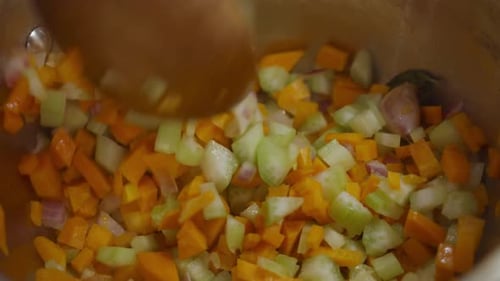Stirring vegetable mix inside cooking pot with a wooden spoon. Close up shot. Slow motion