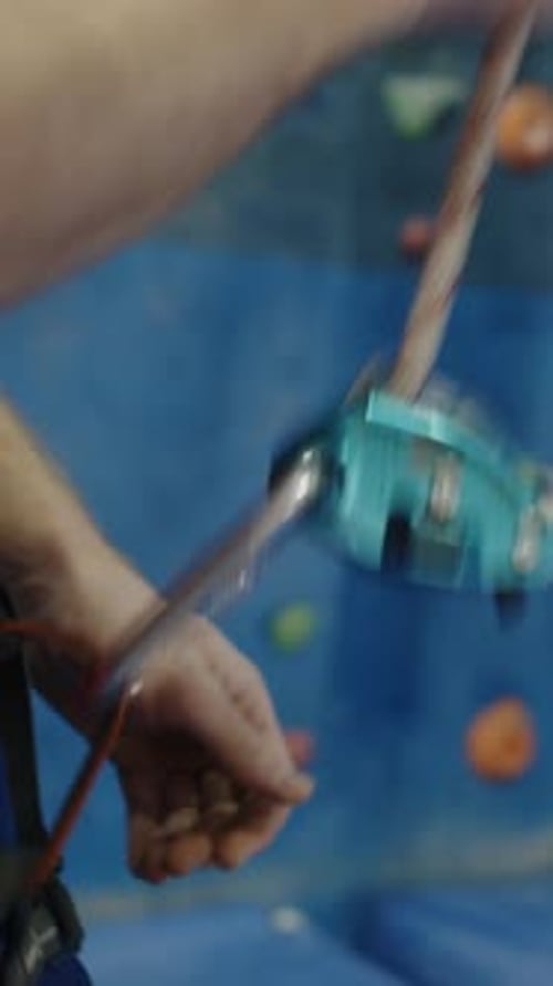 Mãos de homem prendendo corda ao cinto de escalada na academia