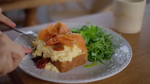 A Woman in a Cafe Eats Scramble Eggs Bread and Salmon Closeup Slow Motion