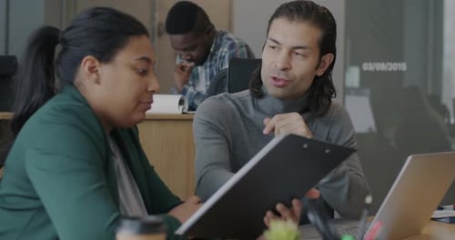 Businesswoman and Man Talking Looking at Documents and Laptop Screen Sitting at Desk in Office