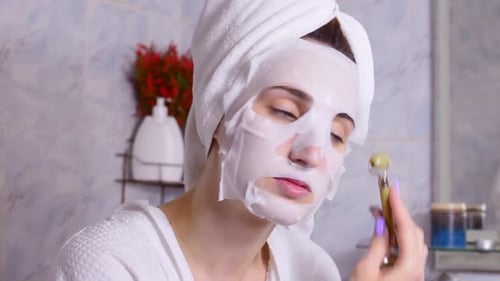 Woman Applying Face Mask and Jade Facial Roller