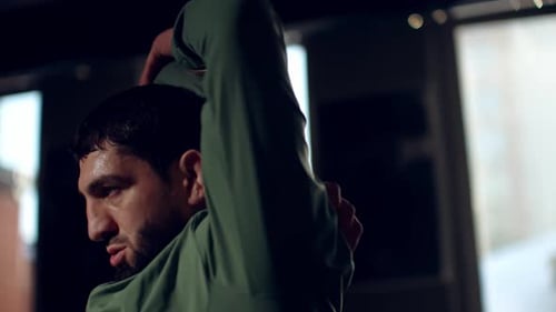 Male Athlete in Green Tracksuit Stretching Arms Warming Up with Intense Focus Before Gym Session