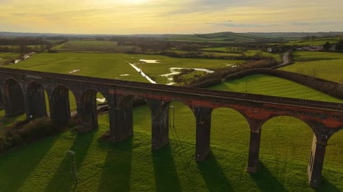 Historic Railway Viaduct Standing Over Green Fields Under Golden Evening Sky Aerial Perspective of