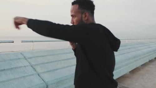 Young athlete boxer practicing punching technique while standing on the embankment