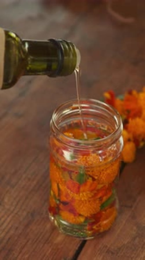 Pouring Olive Oil Generously Over Vibrant Edible Flowers Arranged in a Beautiful Glass Jar