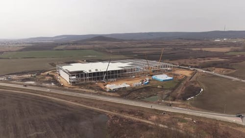 Drone view of a large industrial warehouse under construction surrounded by open fields and
