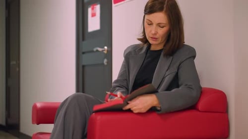 Businesswoman Sitting in Office Reviewing Documents in Notebook