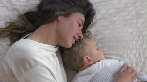 Authentic shot of young mother is caressing her toddler baby boy while sleeping by day on bed with