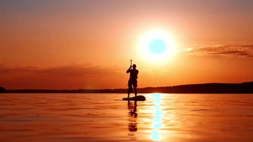 Man Paddle Boarding On Water at Sunset