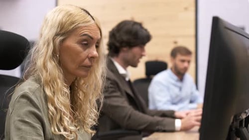 Businesswoman Using Computer with Colleagues Talking in Background