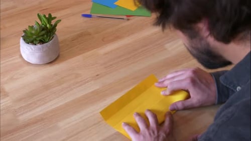 Rear view time lapse of male creating colourful origami paper sheet folding artwork