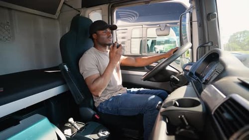 African American Truck Driver Sitting in Cab Speaks on the Radio Walkie Talkie