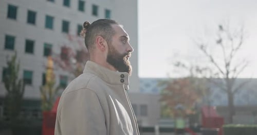 A Young Man with a Stylish Trendy Hairstyle and Beard in Casual Clothes Stands on the Street in the