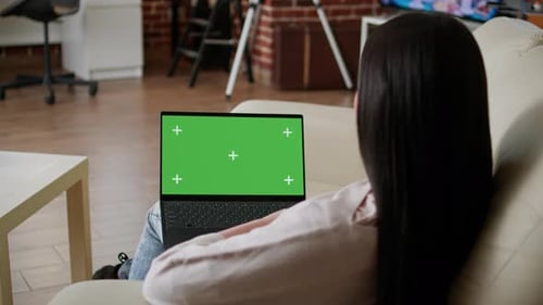 Woman Sitting on Couch Inside Apartment with Portable Computer Having Green Screen