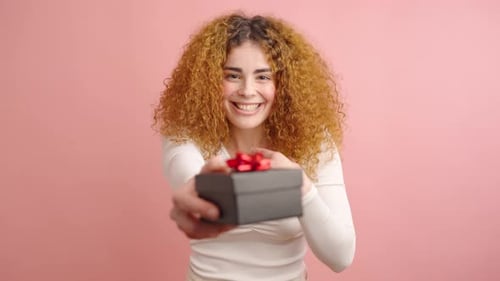 Smiling Young Woman Receiving Gift Box in Pink Studio