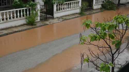 Dirty Water Floods Asphalt Street in Town on Rainy Day