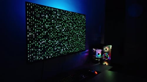 Dark Room with Computer Setup, Large Monitor Displaying Green Matrix Code, and Colorful LED Lighting