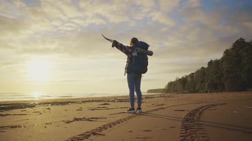 Backpacker on Beach at Sunrise with Arms Outstretched