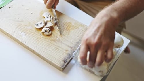 Man cuts fresh white mushrooms on wooden board