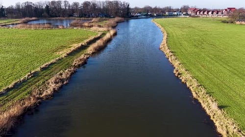 Aerial view of a calm canal running between grassy fields, with reeds along the bank, fenced pasture