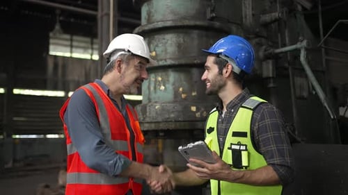 Blue collar workers work together at metal factory.