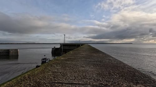 Low perspective view along concrete ocean pier as clouds drift overhead
