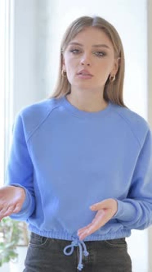 Mujer haciendo un chat de vídeo en línea mientras está de pie en la ventana, vídeo vertical