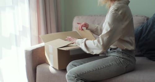 Woman Unpacking a Cardboard Box on Sofa