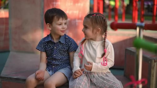Charming Little Girl Taking Hand of Smiling Boy Sitting with Friend on Playground Portrait of Happy