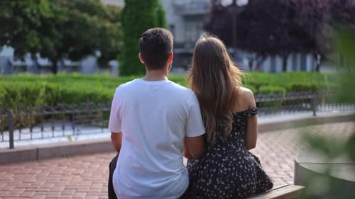 Back View Happy Relaxed Couple Sitting on Bench on City Street As Woman Putting Head on Man Shoulder