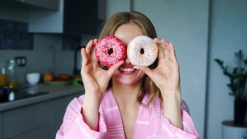 Smiling woman holds up colorful donuts in kitchen