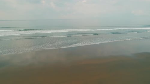 Gentle ocean waves rolling onto a wide reflective sandy beach in morning light