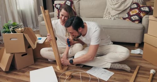 Delighted Handsome Husband with Adorable Wife Trying to Assemble New Modern Floor Lamp Sitting on