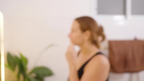 Woman Massaging Under Eye Area with Jade Roller in Bathroom, side view, Morning Routine Concept