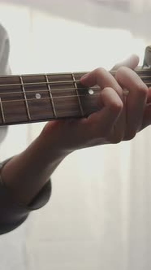 Closeup of Musician Practicing Acoustic Guitar Chords with Decorative Skull Capo Focusing on Hand