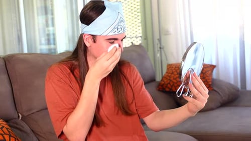 Young Adult Cleans Face Looking at Hand Mirror