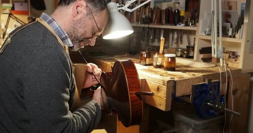 Luthier carefully applying varnish on a new handcrafted violin in his workshop