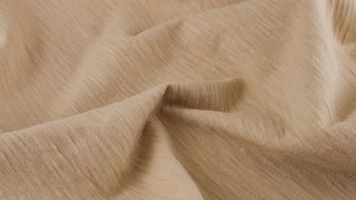 Top view of the soft folds of the thin beige cotton jersey. The textile background rotates