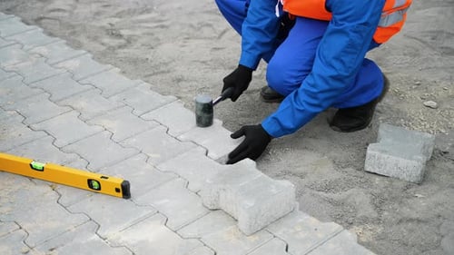 Construction Worker Laying Gray Bricks in Pathway