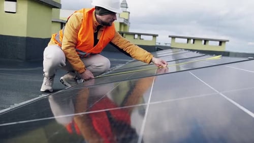 Man Measures Solar Panel Array on Building Rooftop
