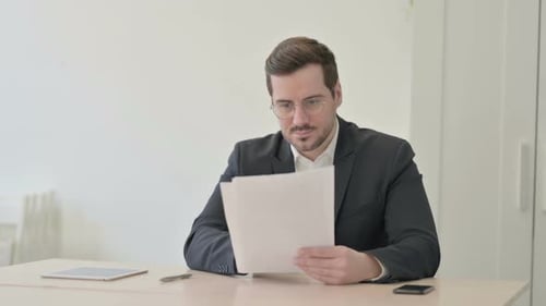 Enthusiastic Man Reading Documents in Office Celebrates Success