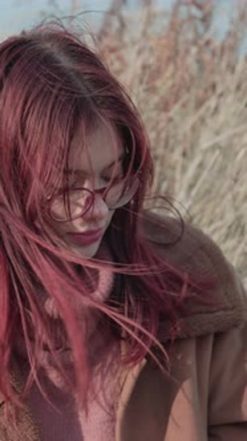 Teenage girl with red hair and glasses, outdoors, looking down pensively