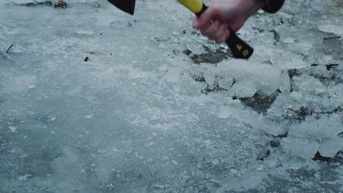 Action-Überlebensszene beim Eishacken, in der eine Axt dickes Eis in der Nähe des Seeufers von Winter spaltet