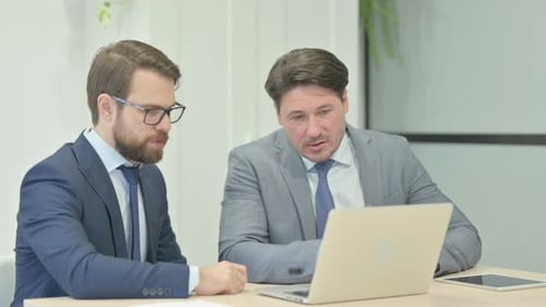 Two Businessmen Discussing Information on Laptop at Desk