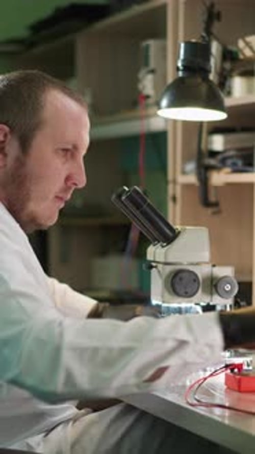 Adult Using Microscope to Examine Circuit Board