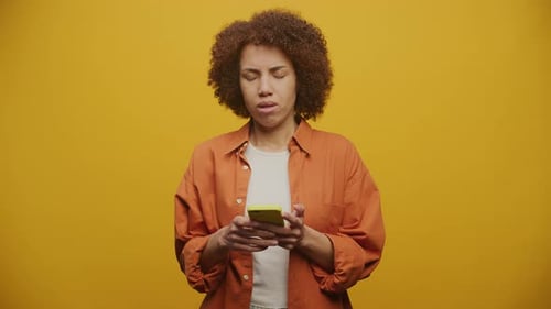 Skeptical Woman Using Cellphone Against Yellow Backdrop
