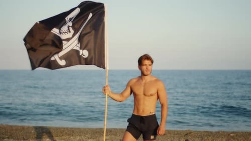 Man Holds Pirate Flag on Beach Shoreline